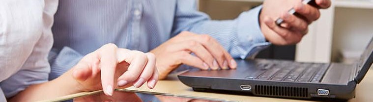 Un-hombre-manejando-su-celular-y-su-laptop-y-una-mujer-manejando-una-tablet